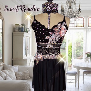 May include: A black dance costume with a sheer top and skirt. The top features a floral design with rhinestones and a black choker with rhinestones. The skirt is a simple black skirt with a sheer overlay.