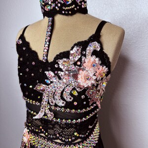 May include: A black dance costume with a lace bodice and skirt. The bodice is embellished with rhinestones and pink flowers. The skirt is also embellished with rhinestones.