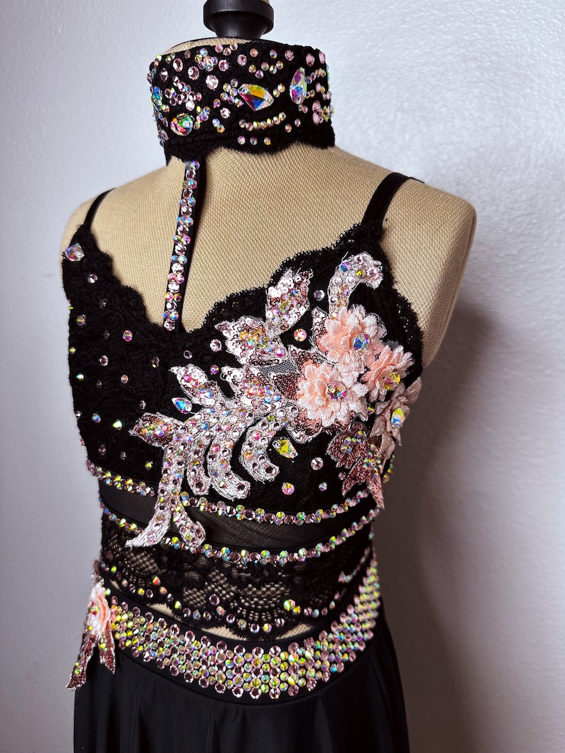 May include: A black dance costume with a lace bodice and skirt. The bodice is embellished with rhinestones and pink flowers. The skirt is also embellished with rhinestones.