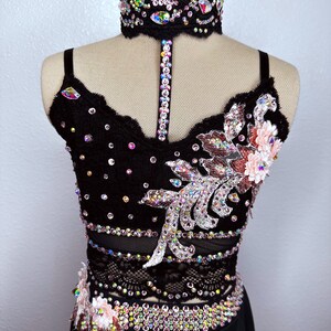 May include: A black dance costume with a lace bodice and skirt. The bodice is embellished with rhinestones and a floral design. The skirt is a simple black skirt.