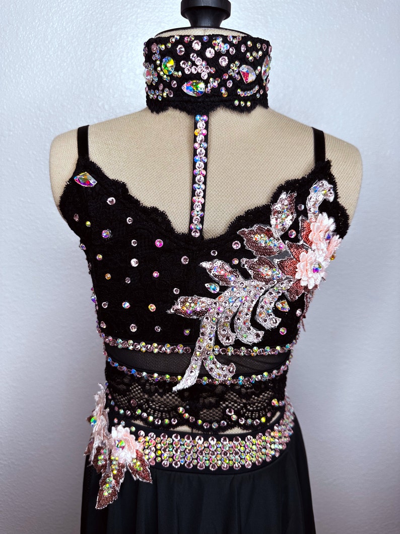 May include: A black dance costume with a lace bodice and skirt. The bodice is embellished with rhinestones and a floral design. The skirt is a simple black skirt.