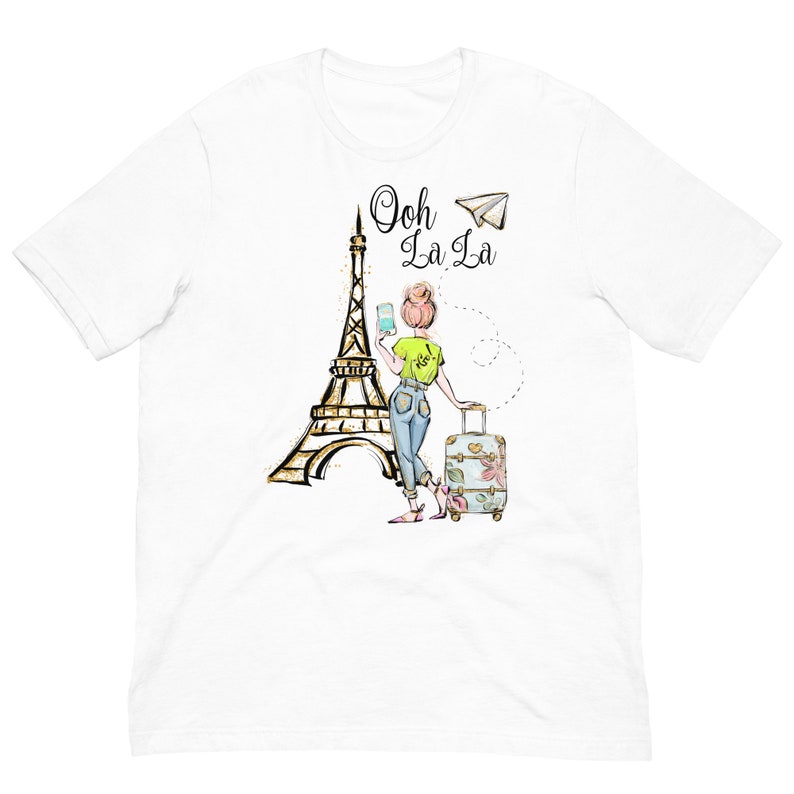 Op de afbeelding: Wit T-shirt met een afbeelding van een vrouw die voor de Eiffeltoren staat met een koffer en een telefoon. De tekst "Ooh La La" staat boven de afbeelding.