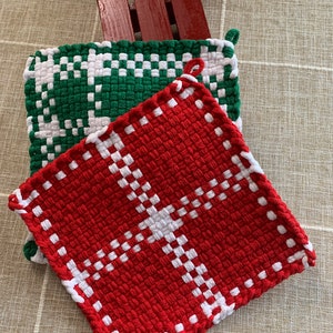 May include: Two woven pot holders, one red and white and one green and white. The pot holders are made with a woven pattern and have a square shape.