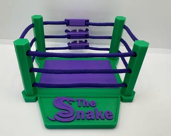 May include: A green and purple wrestling ring with a purple rope and a purple snake logo on the base that says "The Snake".