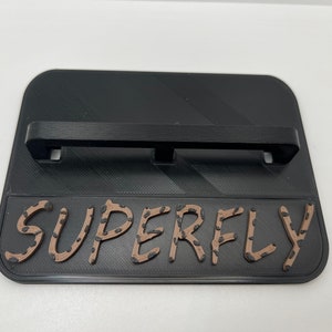 May include: Black plastic wall mount with a horizontal bar and the word "SUPERFLY" printed in brown letters with small brown dots.