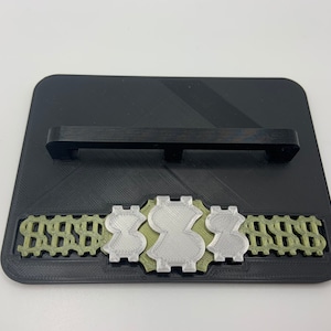 May include: A black rectangular display stand with a silver and green dollar sign design. The stand has a black handle on the top.