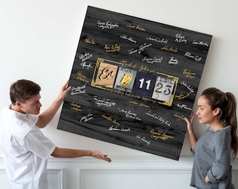May include: A square wall art piece featuring a dark gray wood grain background with numerous handwritten signatures in gold and white ink. A central rectangular gold frame displays the text Est. 12 11 23 with decorative accents.