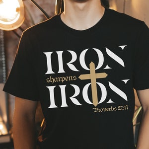 May include: A black t-shirt with a white graphic design that reads "Iron sharpens Iron" with a gold cross and the text "Proverbs 27:17".