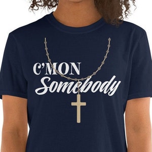 K&ouml;nnte beinhalten: Ein marineblaues T-Shirt mit dem Text "C'mon Somebody" in wei&szlig;en Buchstaben und einem goldenen Kreuzanh&auml;nger an einer Kette.
