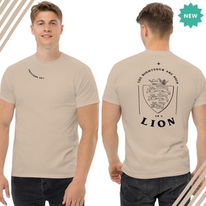 May include: A beige t-shirt with a black graphic on the back that says "The Righteous Are Bold As A Lion" with a crest featuring a lion. The front of the shirt has the text "Proverbs 28:1" in black.