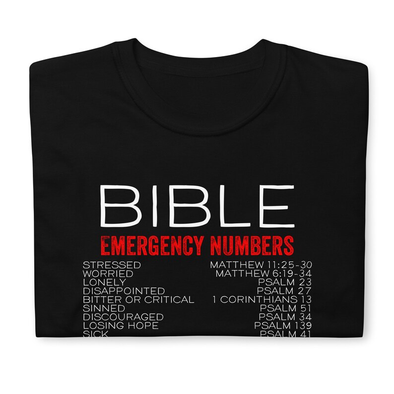 Puede incluir: Camiseta negra con texto blanco que dice "BIBLE EMERGENCY NUMBERS". El texto est&aacute; en negrita, sin serifas. Debajo del texto hay una lista de palabras en rojo, como "estresado", "preocupado", "solo" y "decepcionado", emparejadas con vers&iacute;culos b&iacute;blicos correspondientes en negro.