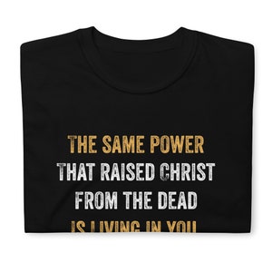 May include: Black t-shirt with the text "THE SAME POWER THAT RAISED CHRIST FROM THE DEAD IS LIVING IN YOU" in yellow.