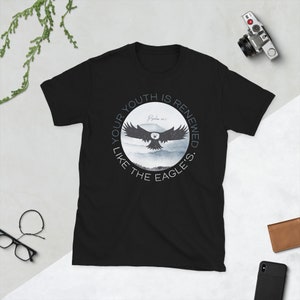 Könnte beinhalten: Schwarzes T-Shirt mit einem runden Grafikdesign, das einen schwebenden Adler, einen Aquarellhintergrund und den Text "Your youth is renewed like the eagle's. Psalm 103:5" zeigt.