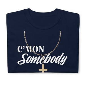K&ouml;nnte beinhalten: Ein marineblaues T-Shirt mit dem Text "C'mon Somebody" in wei&szlig;en Buchstaben. Ein braunes Rosenkranz mit einem goldenen Kreuz h&auml;ngt unter dem Text.