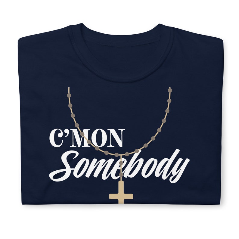 K&ouml;nnte beinhalten: Ein marineblaues T-Shirt mit dem Text "C'mon Somebody" in wei&szlig;en Buchstaben. Ein braunes Rosenkranz mit einem goldenen Kreuz h&auml;ngt unter dem Text.