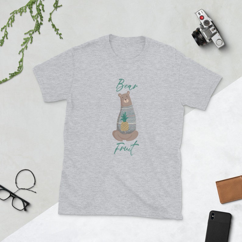 May include: A gray t-shirt with a cartoon bear wearing a sweater and holding a pineapple. The text "Bear Fruit" is printed below the bear.