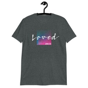 Pu&ograve; includere: Una t-shirt grigio scuro melange con una grafica colorata che dice "loved" in scrittura bianca con "JOHN 3:16" sotto.