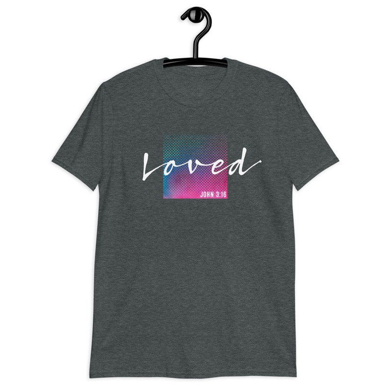 Pu&ograve; includere: Una t-shirt grigio scuro melange con una grafica colorata che dice "loved" in scrittura bianca con "JOHN 3:16" sotto.