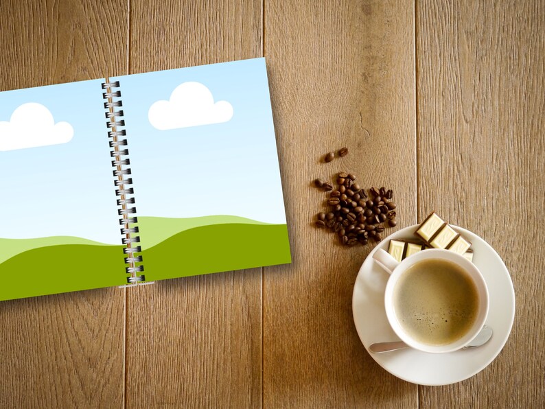 May include: An open spiral-bound notebook with a landscape illustration of green hills, blue sky, and white clouds. A cup of coffee, a saucer, a spoon, and pieces of chocolate are on a wooden surface. Coffee beans are scattered nearby.