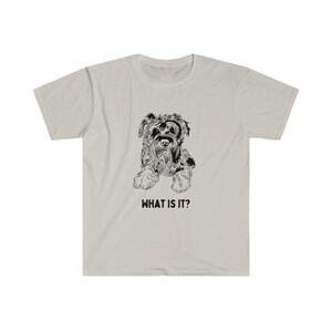 May include: A light grey t-shirt with a black and white illustration of a small dog. The text "WHAT IS IT?" is printed below the dog.