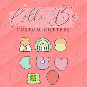 May include: Nine cookie cutters in various shapes and colors, including a rainbow, a pot of gold, a shamrock, a heart, a horseshoe, a crescent moon, a star, and a balloon. The cookie cutters are arranged in two rows on a pink background with the text "Lolli B's CUSTOM CUTTERS".