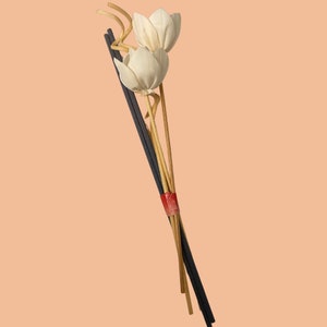 May include: A bouquet of white fabric flowers with brown stems and black sticks tied together with a red ribbon.