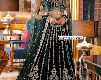 May include: A woman wearing a dark green velvet lehenga with silver embroidery and a matching sheer dupatta. The lehenga has a floral design and the dupatta is decorated with small silver dots.