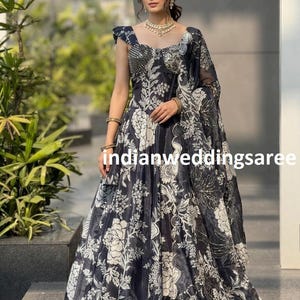 May include: A dark navy blue gown with a white floral pattern and a matching sheer shawl. The gown features a square neckline and cap sleeves. The text "indianweddingsaree" is visible on the gown.