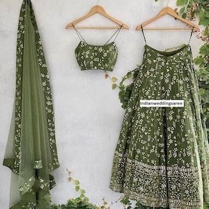 Puede incluir: Un lehenga verde bordado con un top corto verde a juego y una dupatta transparente. El lehenga tiene un patrón floral y un borde plateado. El top corto tiene un patrón floral similar. La dupatta es transparente y tiene un borde plateado.