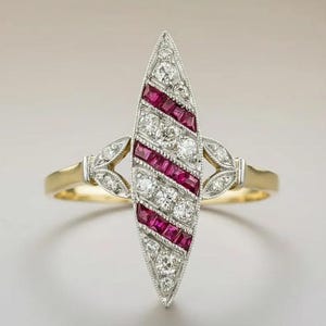Può includere: Un anello a forma di marquise con una fascia in oro giallo e un'incastonatura centrale composta da file diagonali alternate di rubini rossi a taglio quadrato e diamanti rotondi, con piccoli diamanti incastonati sulle spalle metalliche.