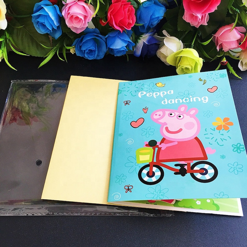 May include: A yellow and blue Peppa Pig themed notebook with a clear plastic cover. The cover features Peppa Pig riding a bicycle with the text "Peppa dancing".