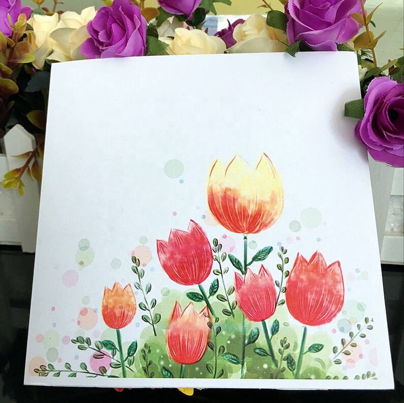 May include: A white card with a watercolor illustration of red, yellow, and orange tulips with green leaves and stems. The background is white with small, light blue circles.
