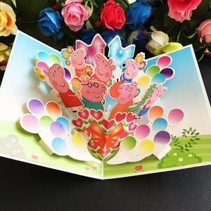 May include: A pop-up card featuring Peppa Pig and her family. The card is decorated with colorful balloons and a bouquet of red hearts with a red bow. The card is perfect for a birthday or other special occasion.