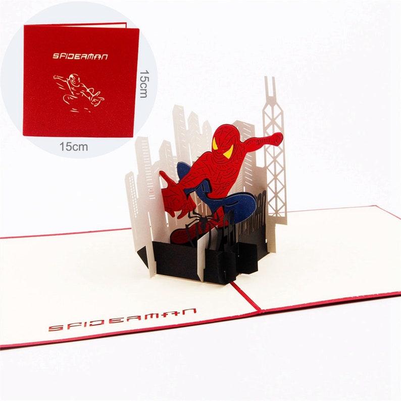 May include: A red and blue 3D pop-up card featuring Spiderman swinging through a cityscape. The card is 15 inches by 15 inches and has a red cover with a white outline of Spiderman.
