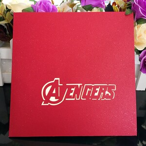 May include: Red card with a white "Avengers" logo. The logo is in a circle with a star inside.