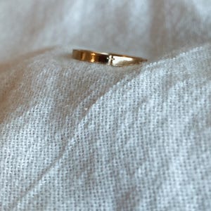 May include: A simple gold band ring with a small cross design.