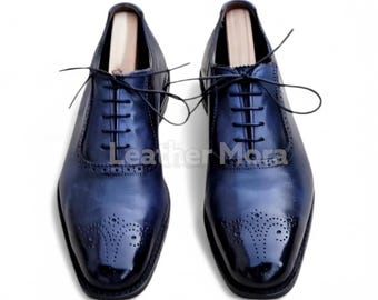 Könnte beinhalten: Ein Paar marineblaue Lederschuhe mit glänzendem Finish. Die Schuhe haben ein klassisches Oxford-Design mit dekorativen Perforationen an der Spitze und einem Schnürverschluss. Der Text "Leather Mora" ist sichtbar.