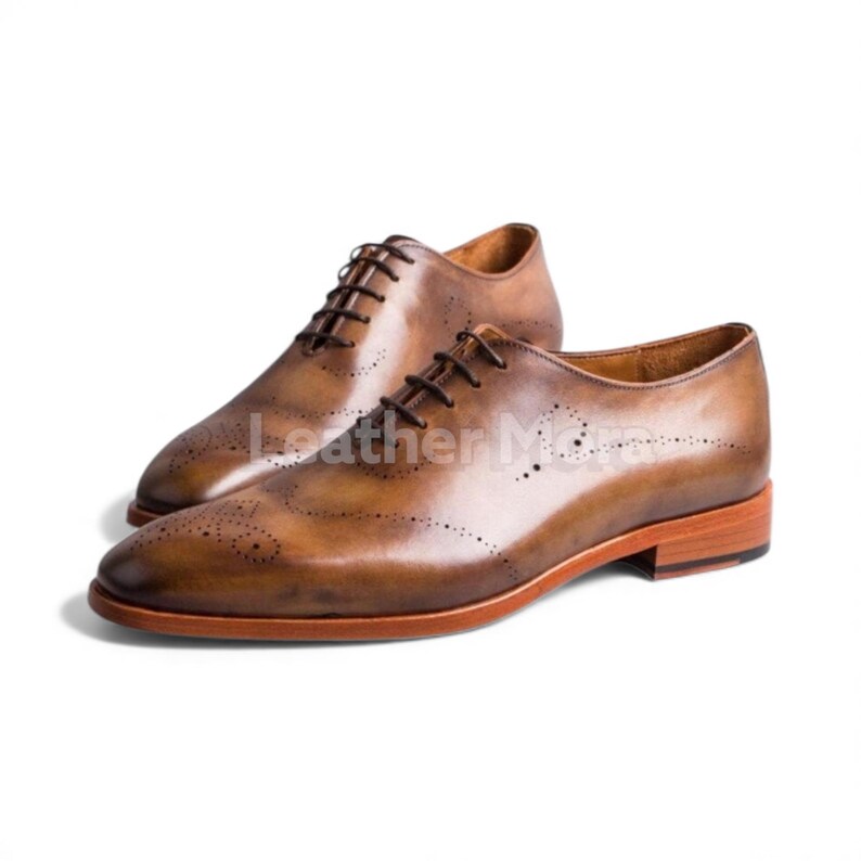 May include: A pair of brown leather Oxford shoes with intricate brogue detailing. The shoes feature a classic lace-up design and a polished finish. The soles have a reddish-brown hue, and the shoes are set against a white background.