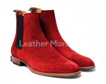 May include: A pair of red suede Chelsea boots with a low heel and elastic side panels. The boots have a leather sole and the text "Leather Mora" is visible on the side.