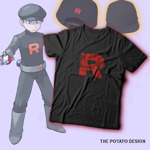 Könnte beinhalten: Ein schwarzes T-Shirt mit einem roten, abgenutzten Buchstaben "R" auf der Vorderseite. Das Shirt befindet sich neben einem Cartoon-Bild eines Charakters, der eine schwarze Kappe mit einem roten "R" trägt. Der Charakter hält einen roten und weißen Pokéball.
