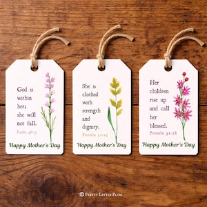 May include: Three white gift tags with floral illustrations and text. Each tag has a different quote and reads "Happy Mother's Day." The tags are tied with twine and set against a wooden background.