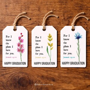 May include: Three white graduation gift tags with watercolor floral designs and the text "For I know the plans I have for you. Jeremiah 29:11. HAPPY GRADUATION." Each tag has a twine string.