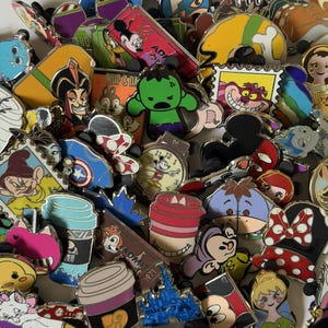 May include: A large collection of colorful metal enamel pins featuring various cartoon characters, including a green superhero, a smiling cat, a clock, coffee cups, and iconic mouse ears, all arranged in a dense, overlapping pile.
