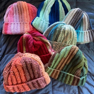 May include: Seven crocheted hats in various colors and patterns, including pink, blue, gray, green, and brown.