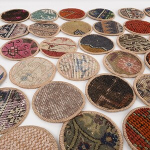 May include: A collection of oval-shaped coasters with a woven rug design. The coasters feature various colors, including red, blue, green, and brown, with a beige border. The coasters are arranged on a white surface.
