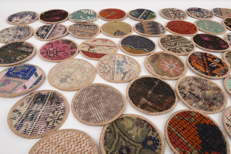 May include: A collection of oval-shaped coasters with a woven rug design. The coasters feature various colors, including red, blue, green, and brown, with a beige border. The coasters are arranged on a white surface.