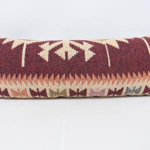 May include: Rectangular decorative pillow with a burgundy background and a geometric pattern in beige, orange, and blue. The pillow has a woven texture and is designed for home decor.