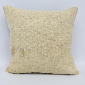May include: A plain off-white square cushion with a woven texture. The cushion is made of natural fibres and has a slightly rough surface.