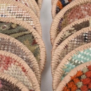 May include: Close-up of several semi-circular rugs with a variety of colors and patterns. The rugs have a beige border and are arranged in a fan-like shape. The colors include pink, green, orange, and brown.