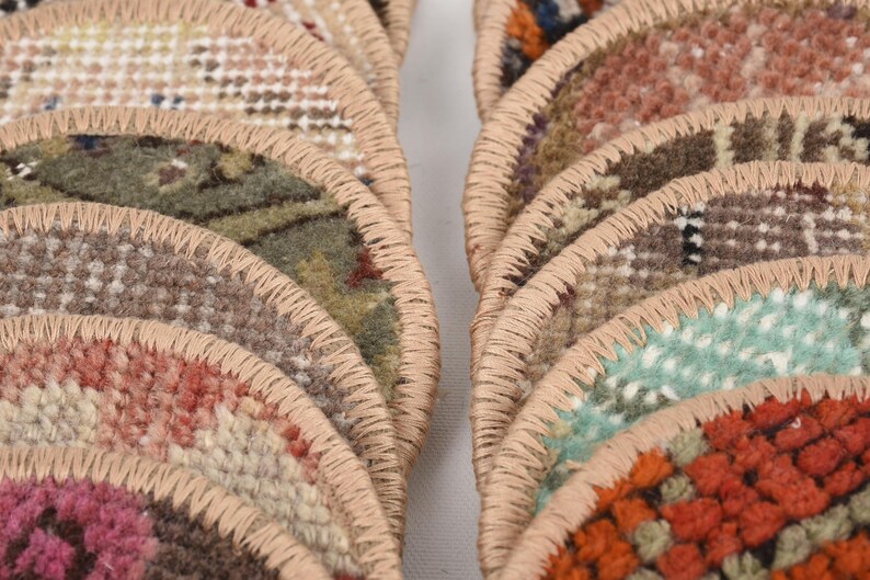 May include: Close-up of several semi-circular rugs with a variety of colors and patterns. The rugs have a beige border and are arranged in a fan-like shape. The colors include pink, green, orange, and brown.